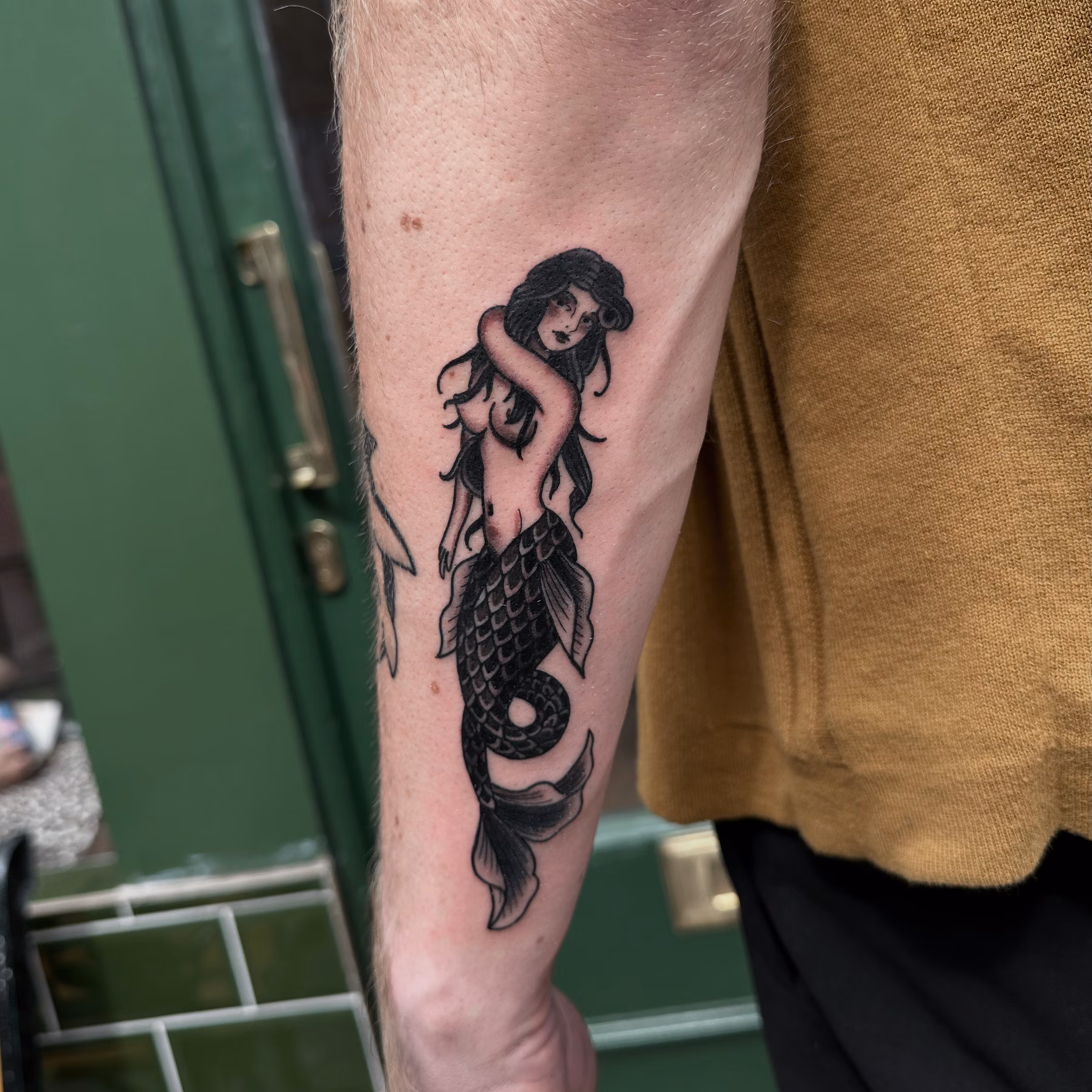 Traditional black and grey mermaid tattoo on a forearm