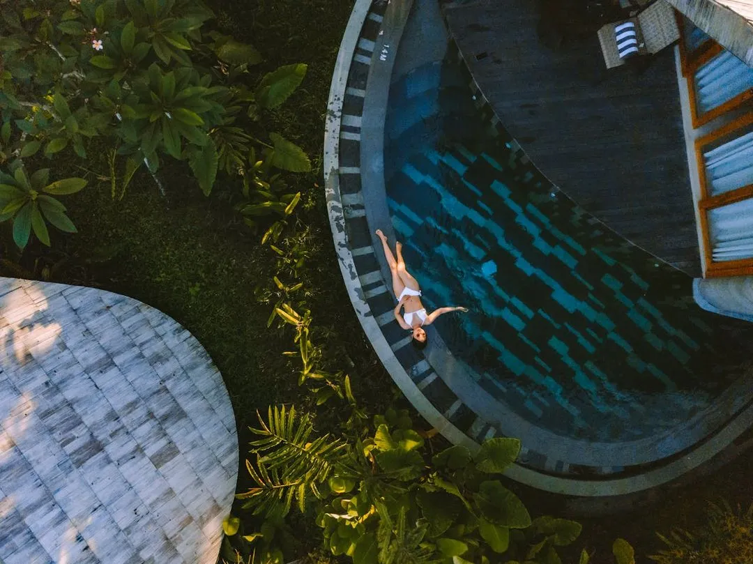 Woman laying down in a swimming pool, with a lot of plants around her.