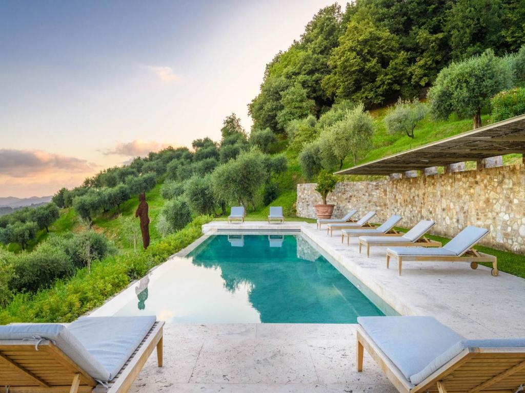 Outdoor pool with lounge chairs on stone deck overlooking green hillside with trees at sunset.
