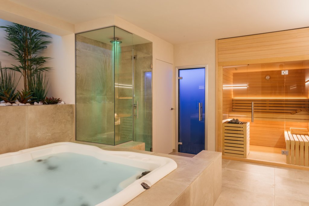Modern spa room with a jacuzzi tub, glass-enclosed shower, and a wooden sauna with seating.