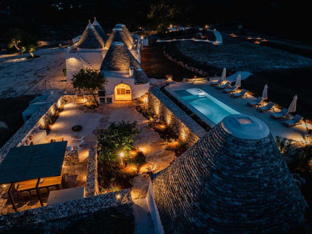 Night view of illuminated trulli houses with a pool and lounge chairs in a stone-walled courtyard.