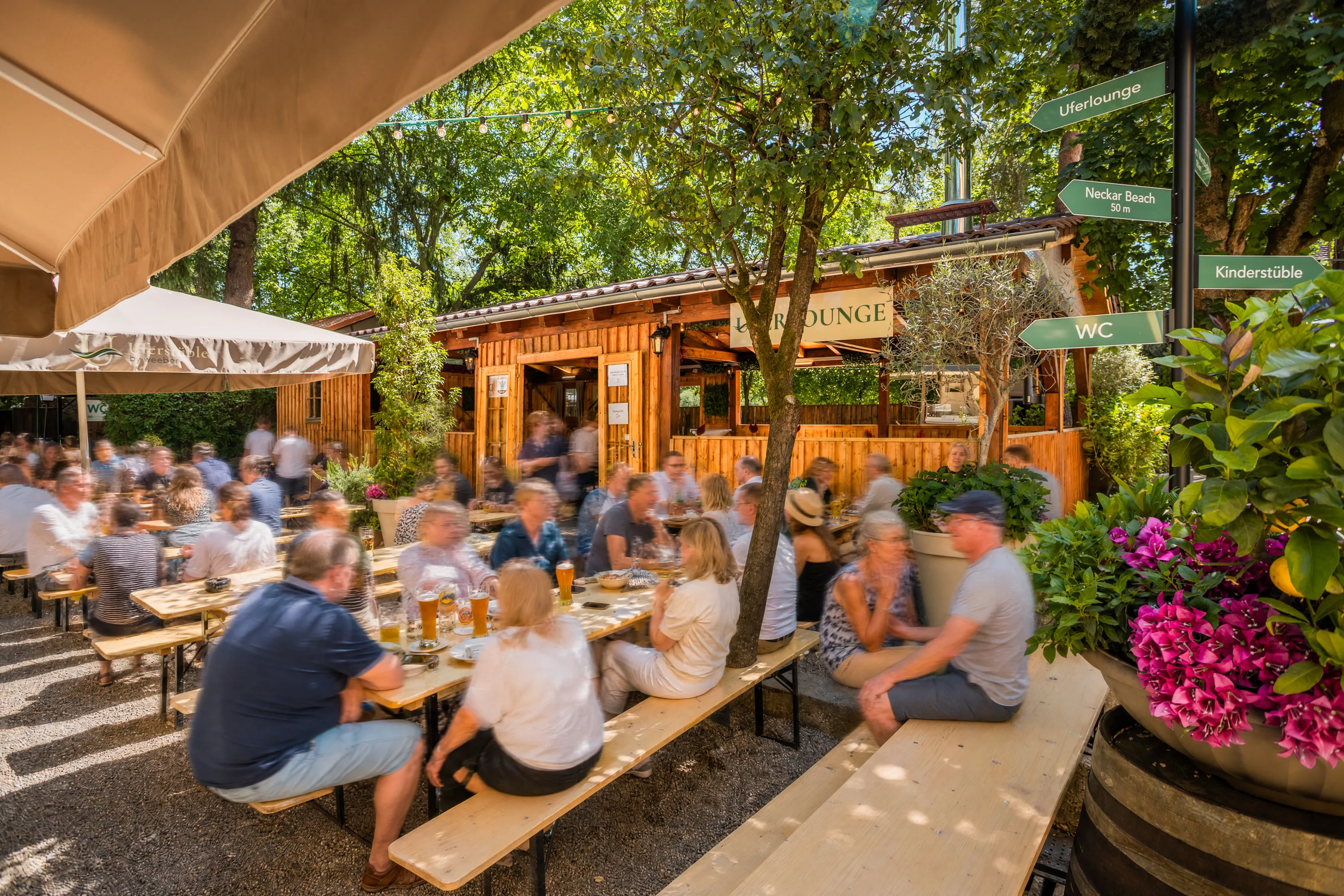 Gäste an Biertischen im Biergarten Uferstüble mit Blick auf die Uferlounge