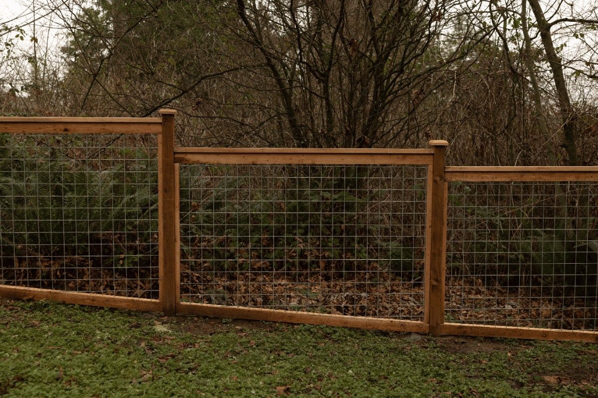 Hog wire fence panels in a cedar frame along a wooded property edge