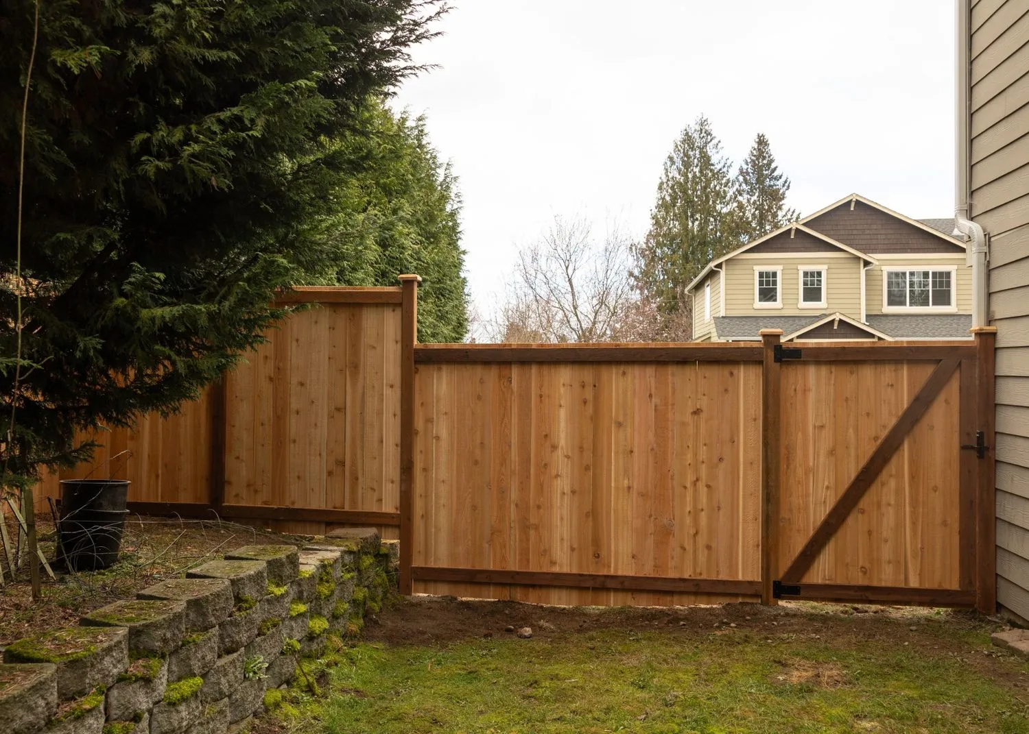 Wooden fence with gate built near a tree and low retaining wall of a Portland backyard