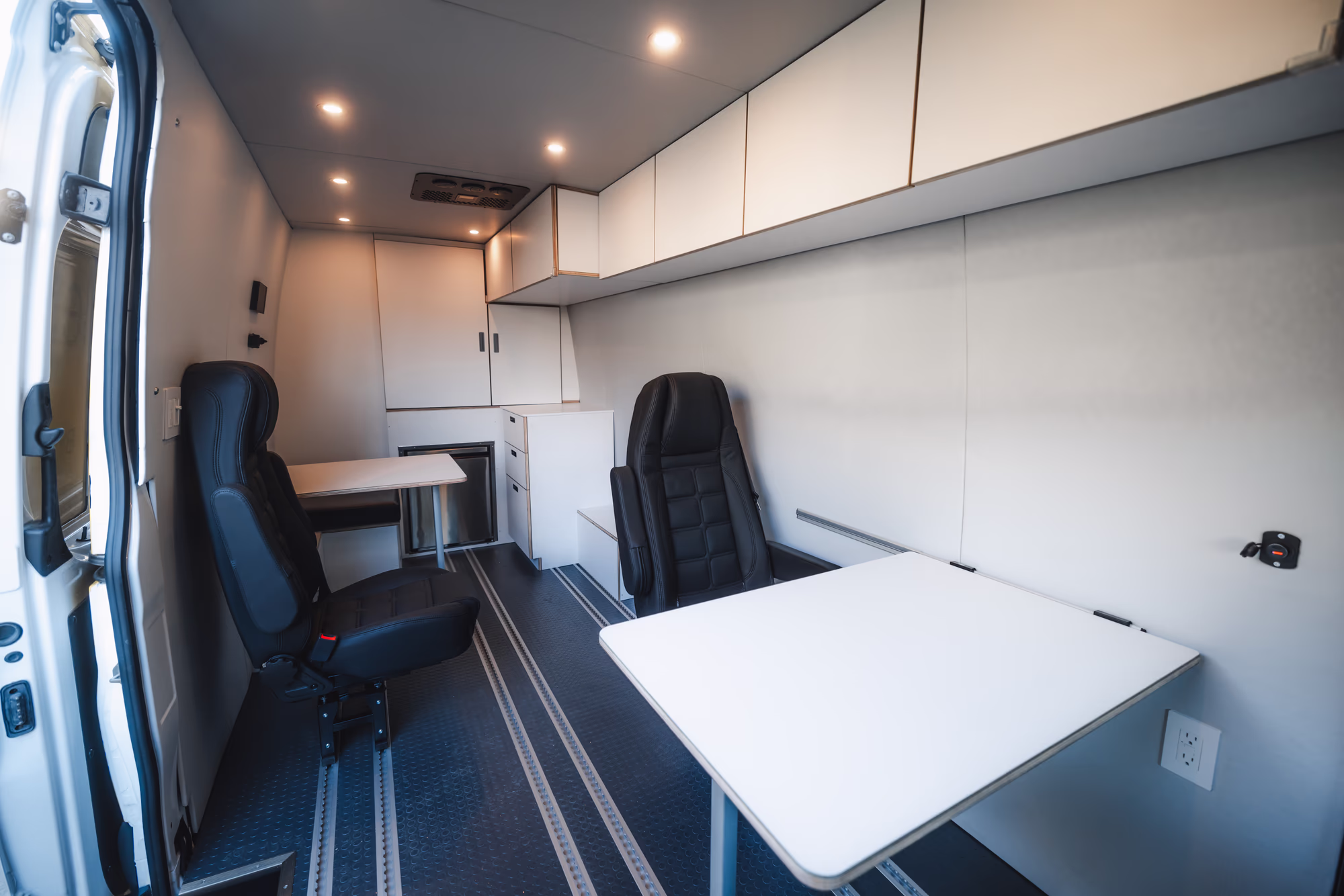 Clean white Sprinter mobile office interior with fold-down desk and two swivel seats