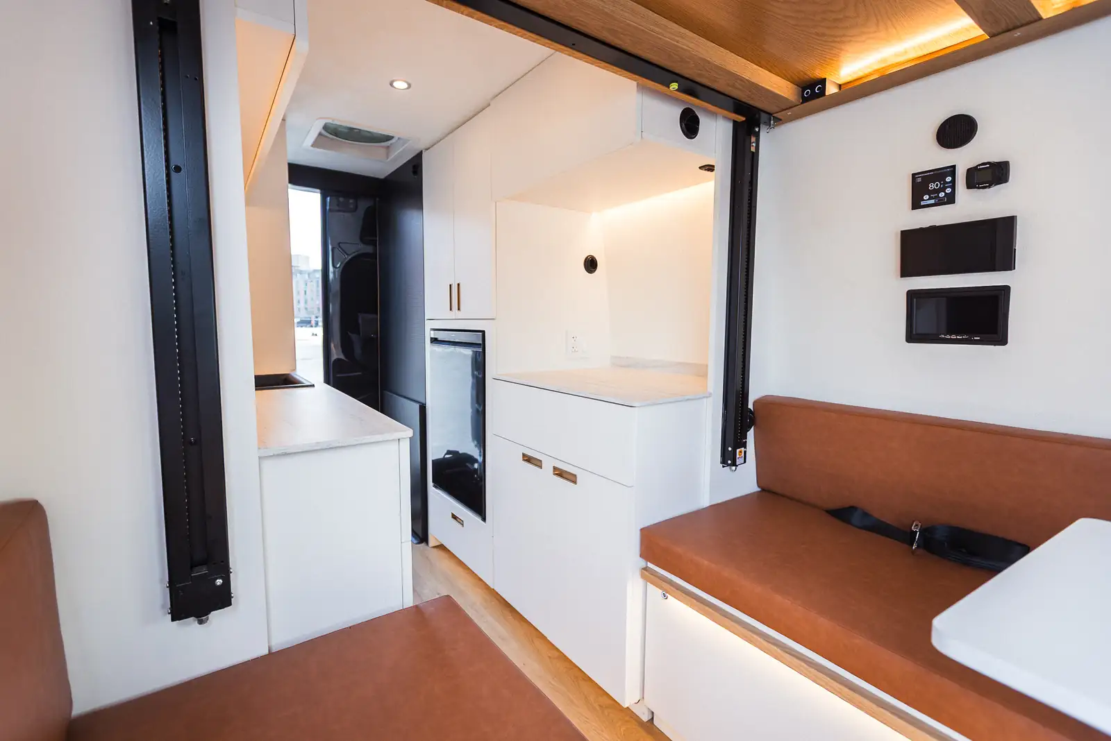 Brooklyn Campervans camper interior with white cabinets, brown leather seats, wood ceiling and rear window
