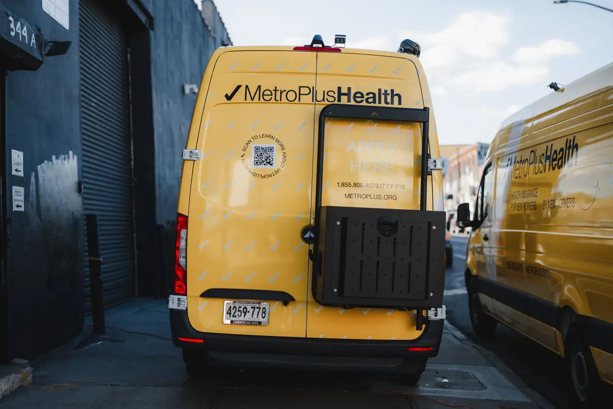 Rear of a yellow MetroPlusHealth Sprinter with a full wrap, QR code and phone number