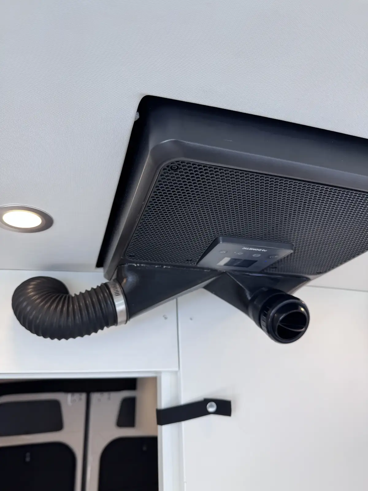 Black ceiling-mounted climate unit with a flexible air duct and a small control display