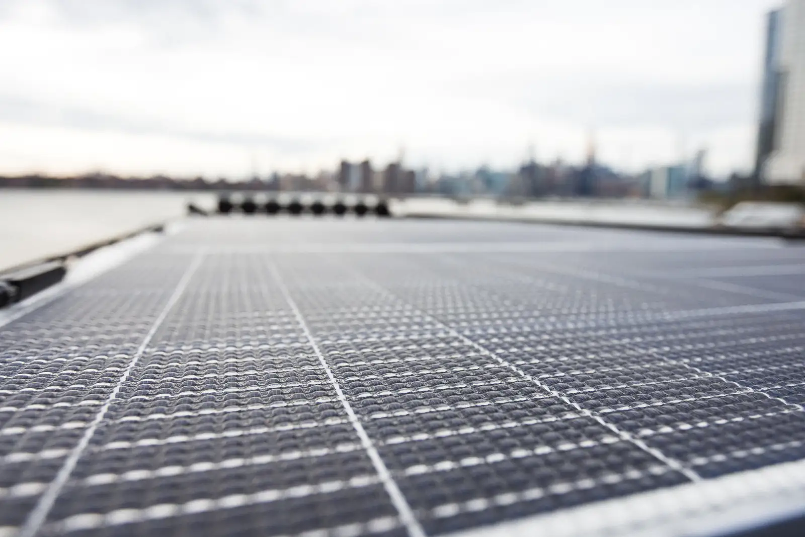 Close-up of flexible solar panels on a van roof, with a city skyline blurred in the background