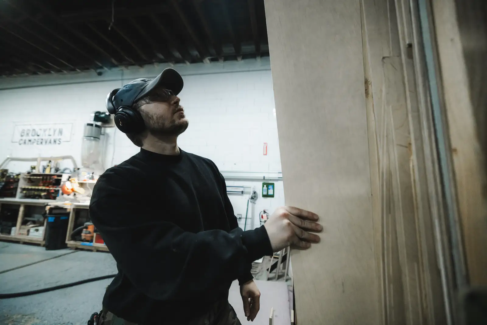 Builder in ear protection steadying a tall plywood panel in the Brooklyn workshop