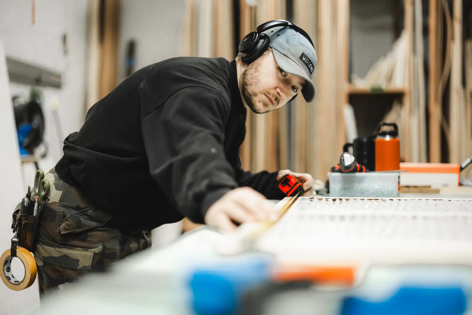 Builder leaning over a workbench to measure and mark a panel with a tape measure