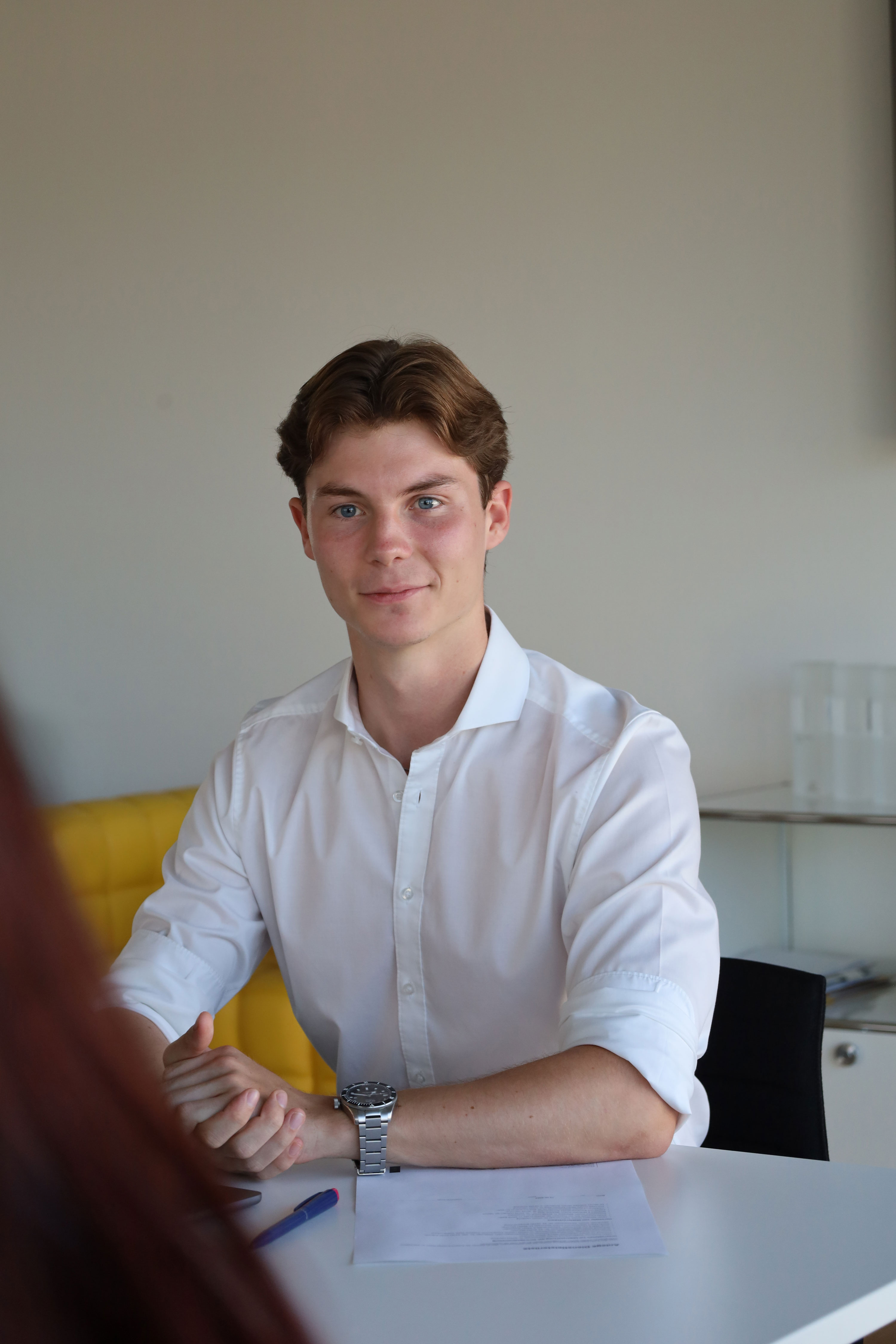 Junger Mann mit weißem Hemd sitzt an einem Tisch mit Dokument und Stift im Büro.