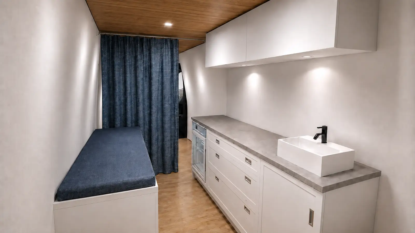 3D rendering of a mobile clinic interior with dark blue exam bench, blue curtain, white cabinets and sink