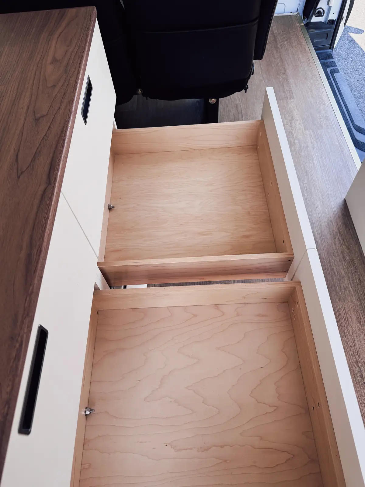 Mercedes Sprinter interior with two walnut folding tables, swiveled front seats and black seats facing them