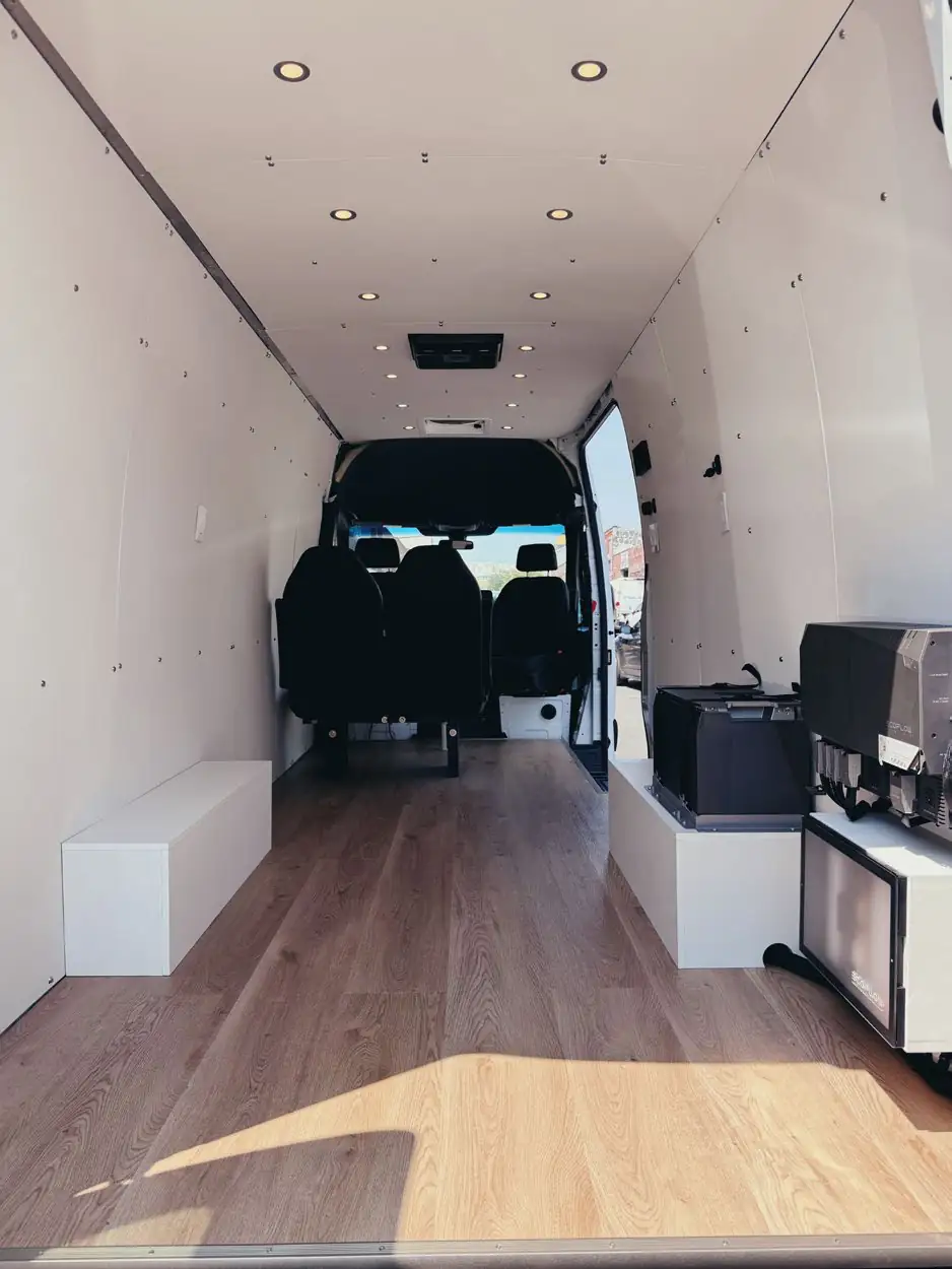 Tall white Mercedes Sprinter interior facing the cab with two black seats, low benches and an EcoFlow battery bank
