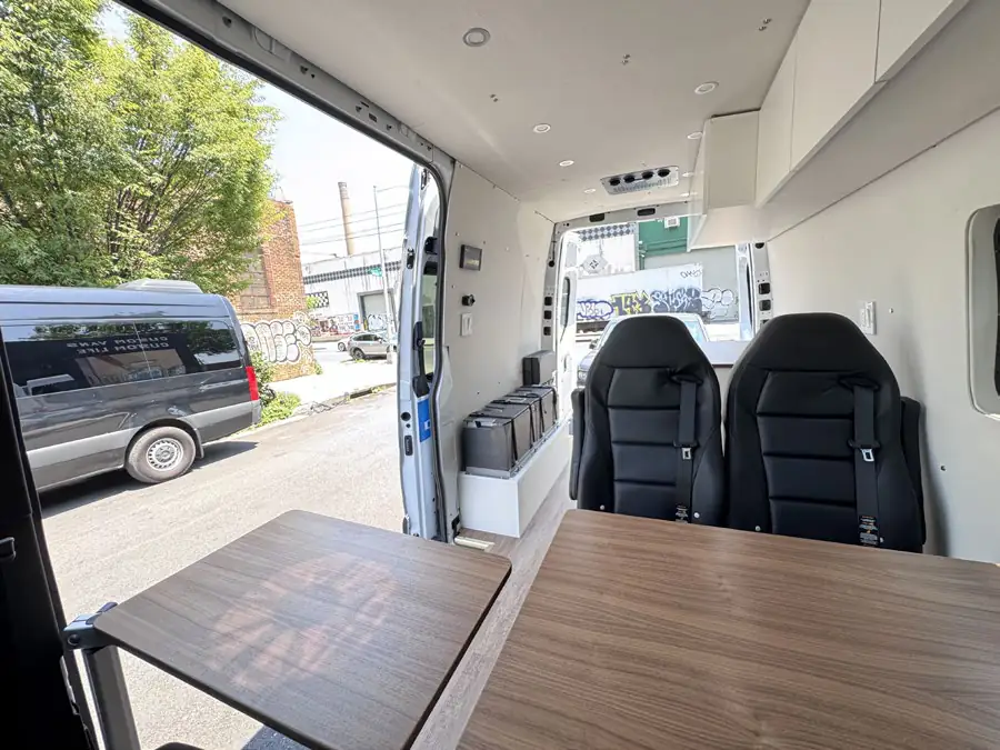 Mercedes Sprinter interior with walnut tables, black leather seats and rear doors open to a graffiti-lined Brooklyn street