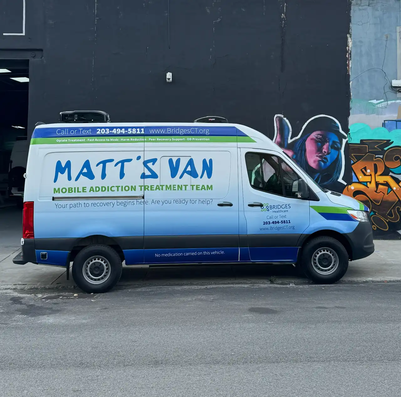 Side view of the Bridges Healthcare MATT'S VAN Mobile Addiction Treatment Team Mercedes Sprinter outside a black shop