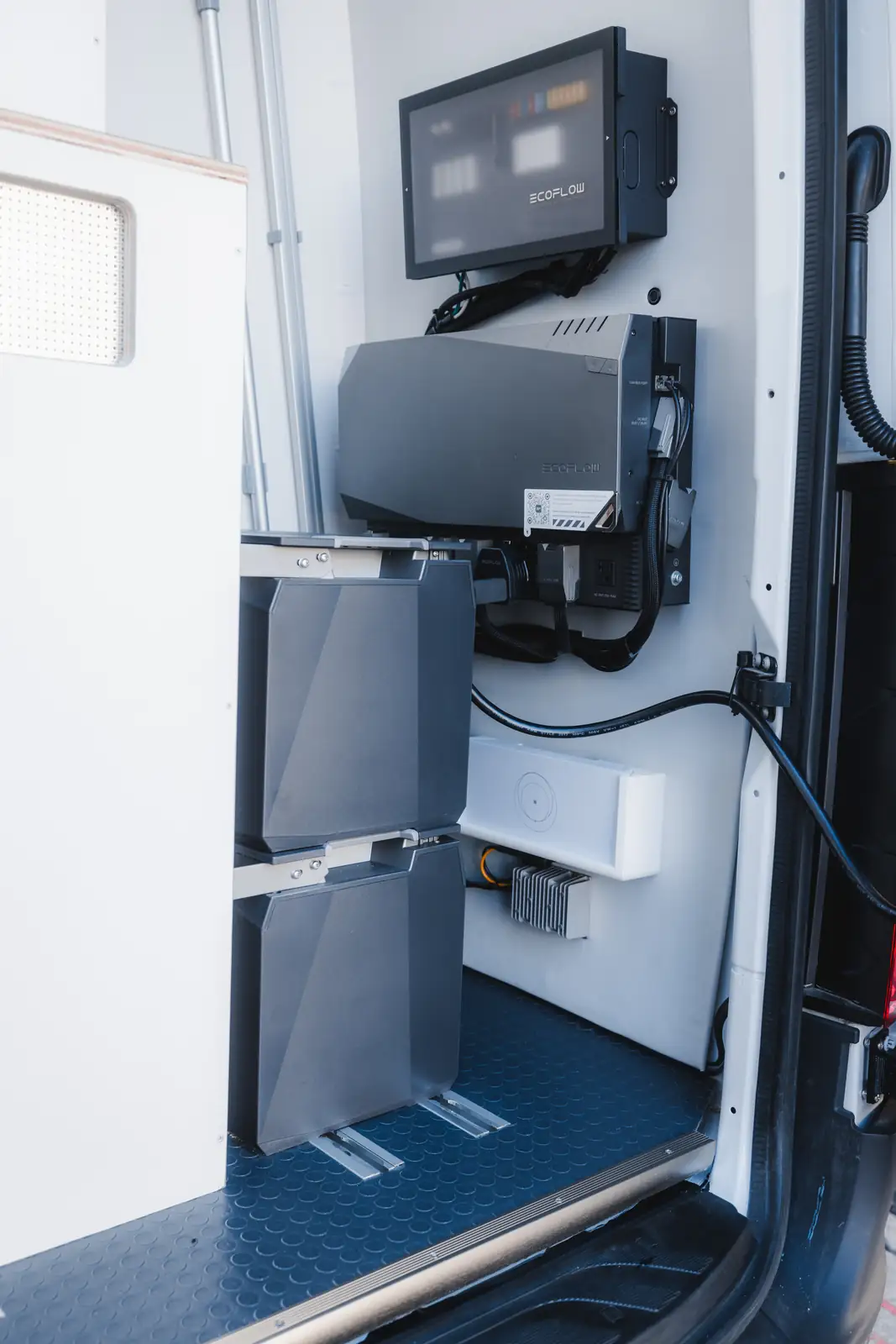 EcoFlow wall monitor, inverter charger and two stacked grey batteries installed by the rear door of a van