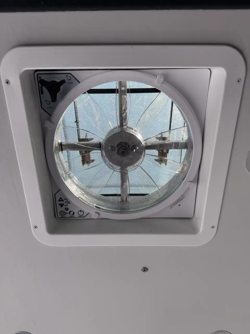 Close-up of a white roof exhaust fan with grille and blades seen from inside a van