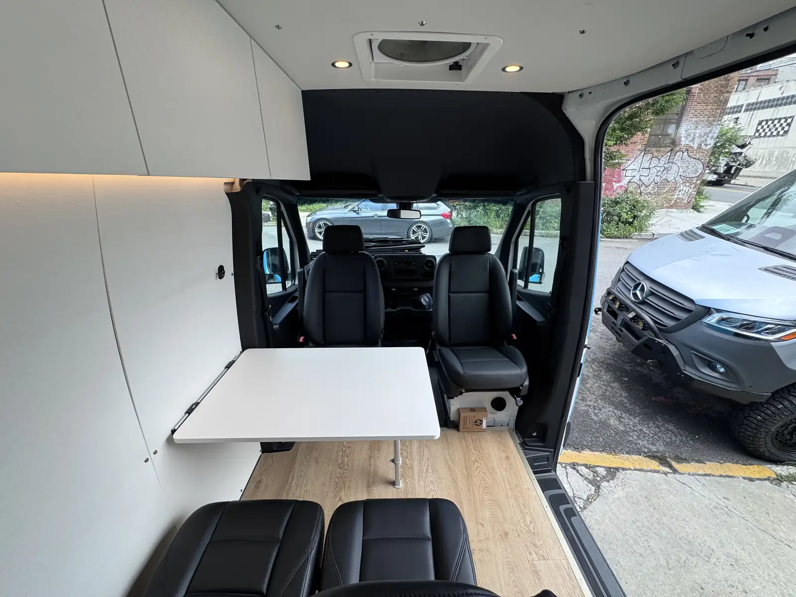Mercedes Sprinter interior looking forward with black swivel seats, white folding table, leather rear seats and roof fan