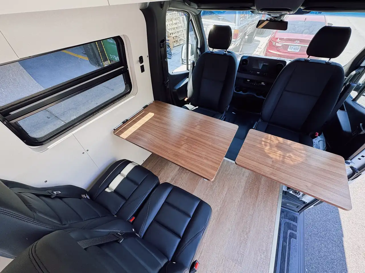 Mercedes Sprinter interior facing the cab with two walnut folding tables, black leather seats and side window with shade
