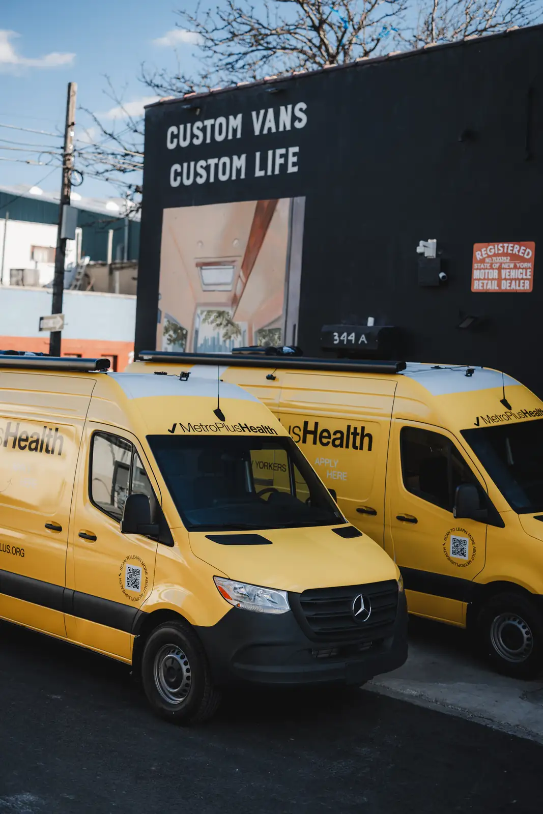 Two yellow MetroPlusHealth Sprinter vans parked in front of the Brooklyn shop