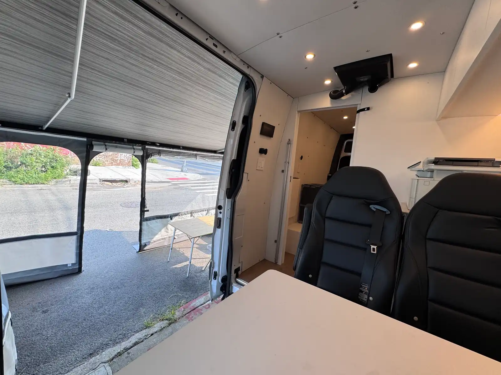 Two black seats and a white table inside the van, facing the open side door and the awning tent