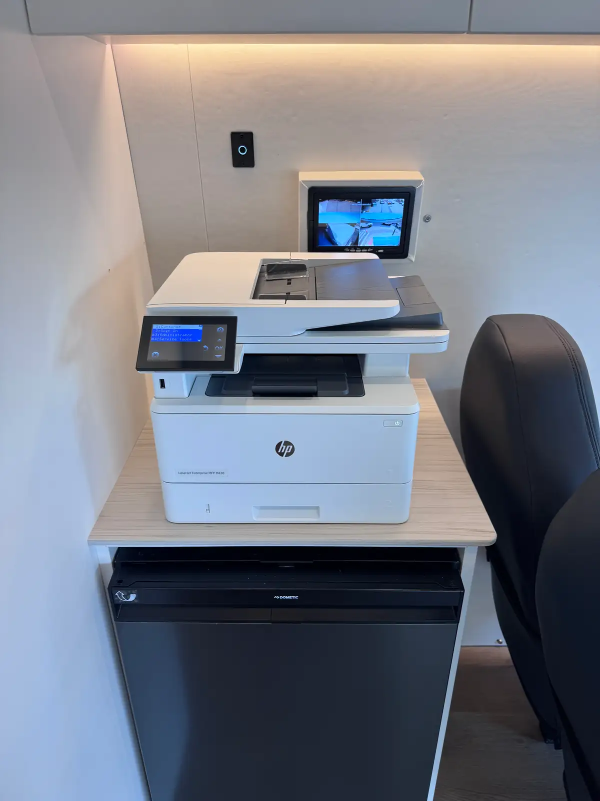 HP printer on a counter above an under-counter fridge, with a wall-mounted control screen