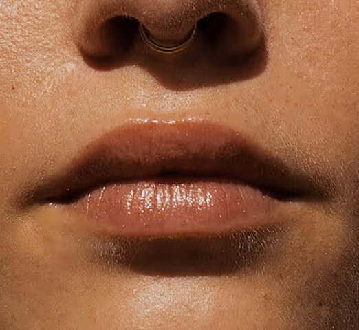 Close-up of a person's lower nose and lips with a gold septum ring and smooth skin.