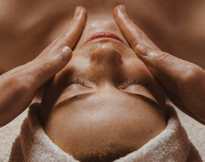 Person receiving a facial massage with hands gently pressing on their face and a towel around the head.