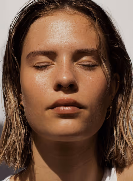 Close-up of a young woman with wet hair and closed eyes facing sunlight.