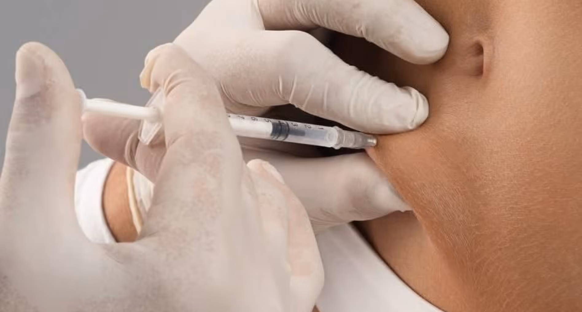 Gloved hand injecting a syringe into the side of a person's lower abdomen near white clothing.
