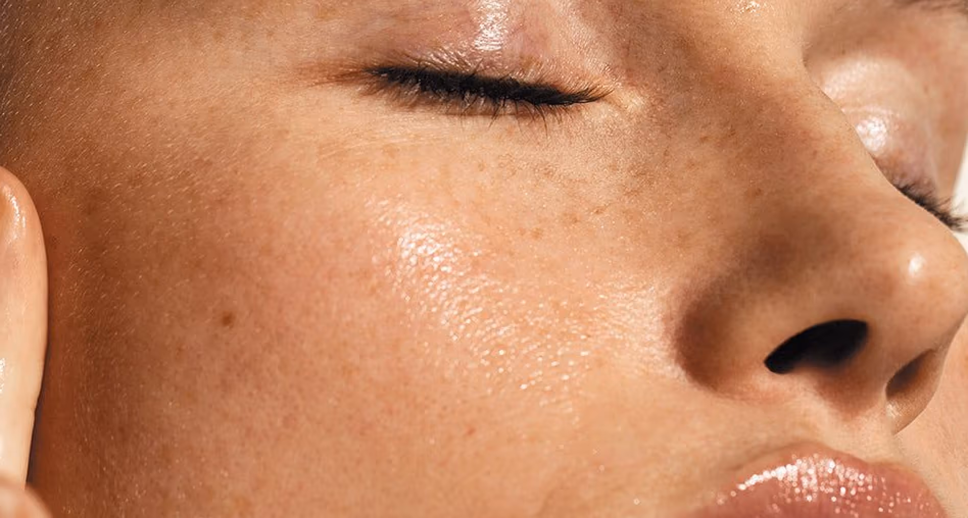 Close-up of a serene person's freckled face with closed eyes and glossy lips.