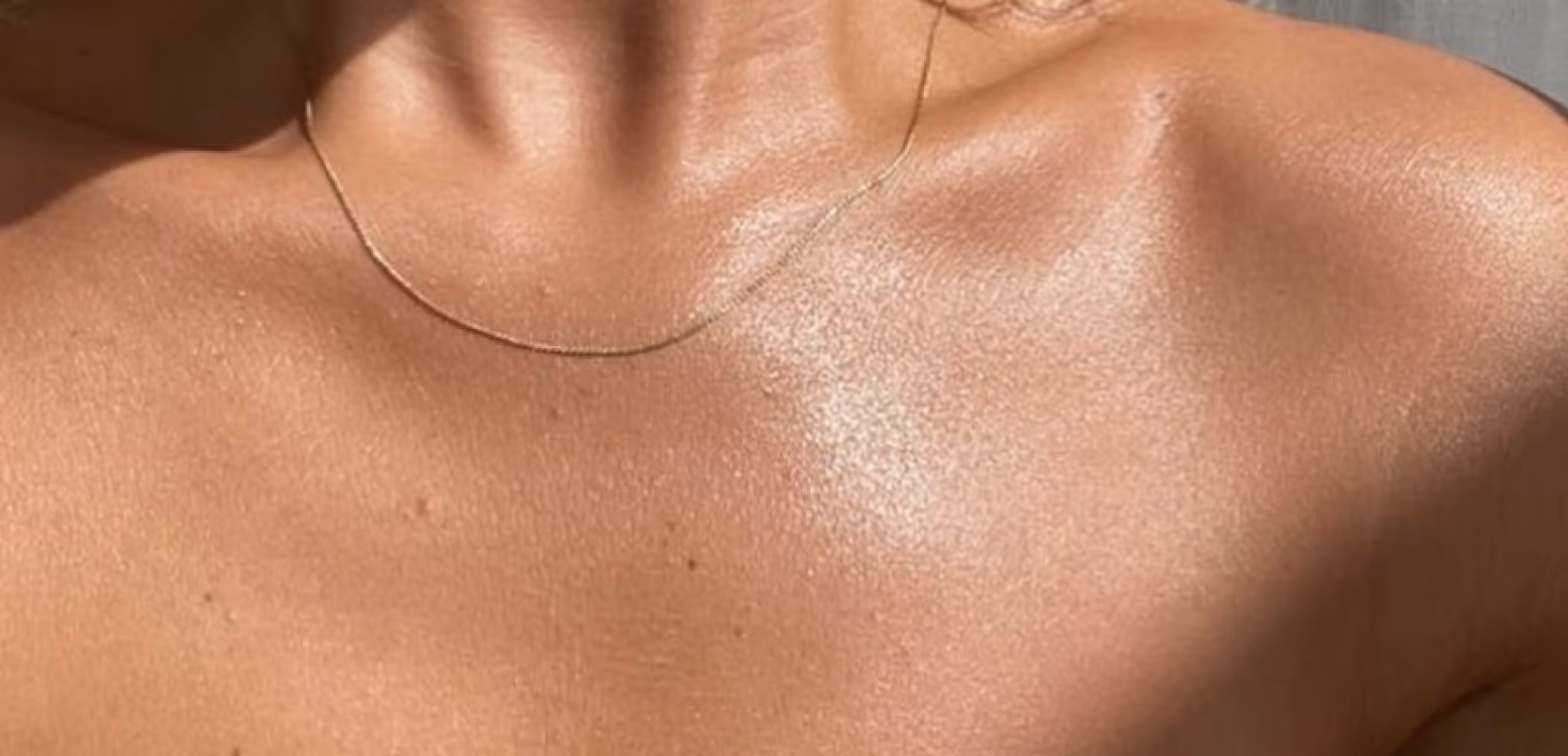 Close-up of sunlit bare shoulders and upper chest with a thin gold necklace.