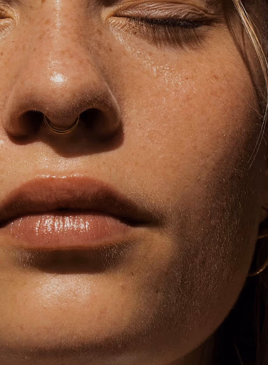 Close-up of a closed-eyed person’s face showing skin texture, lips, nose, and a gold nose ring.