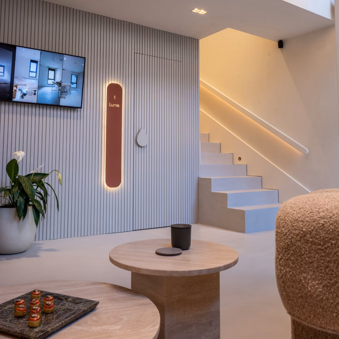 Modern waiting area with three beige armchairs, white side tables, pendant lights, and a staircase leading to an upper floor.
