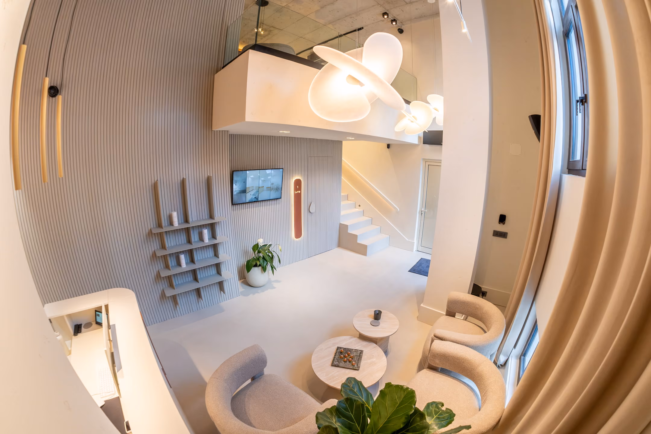 Top-down view of a modern sitting area with large spherical pendant lights, brown armchairs, round marble tables, and a tall vase with dried pampas grass.