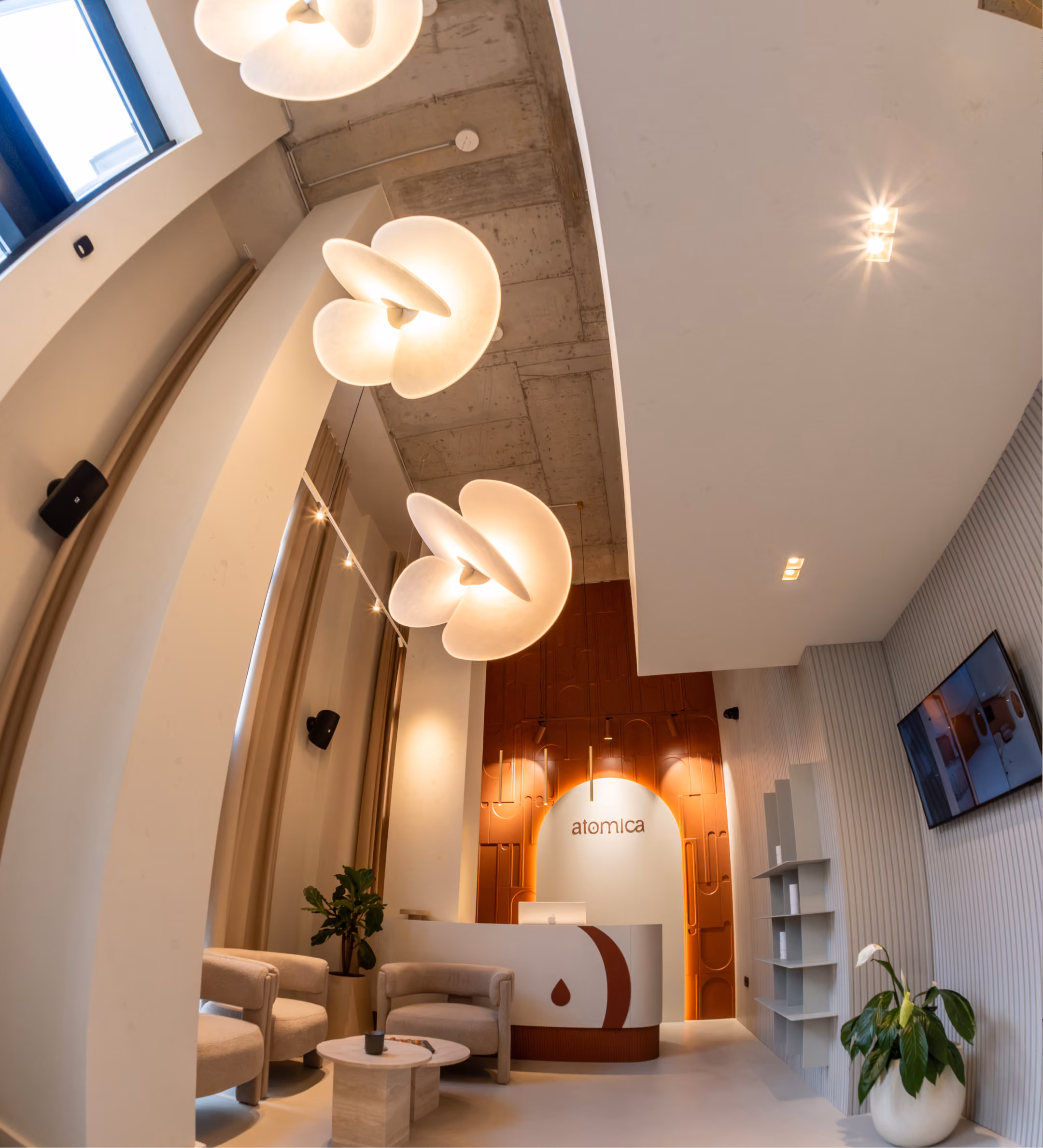 Modern clinic reception area with beige upholstered chairs, marble coffee table, curved reception desk, and accent lighting.