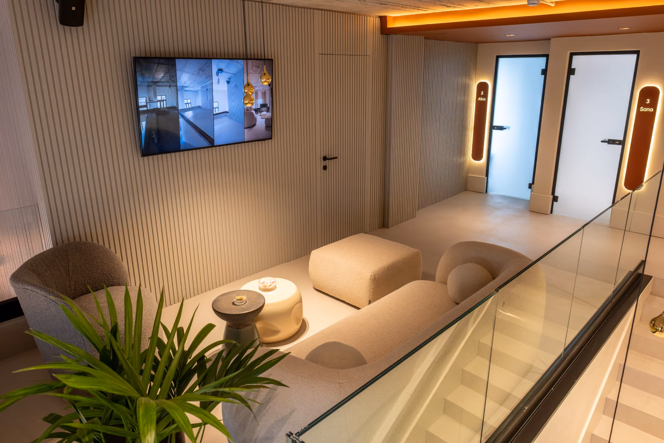 Modern reception area with curved beige desk, three brown chairs, marble coffee table, and a wall sign reading 'Atomica' in a softly lit room with tall curtains and decorative plants.