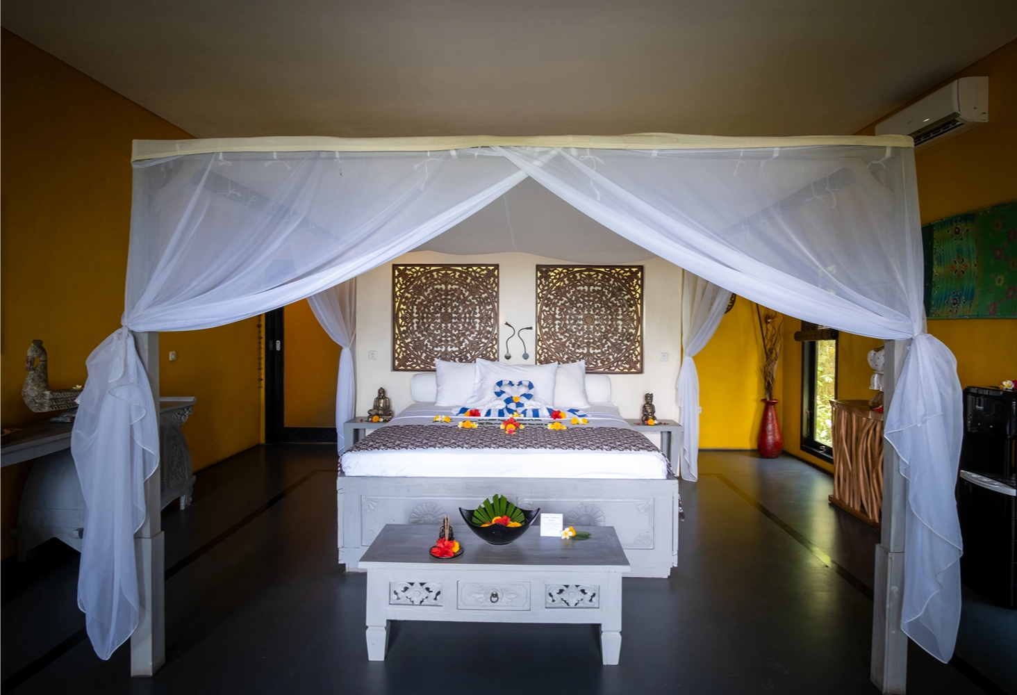 Premium villa with four-poster bed with white sheer curtains, decorative pillows, flower petals, and ornate wall art.