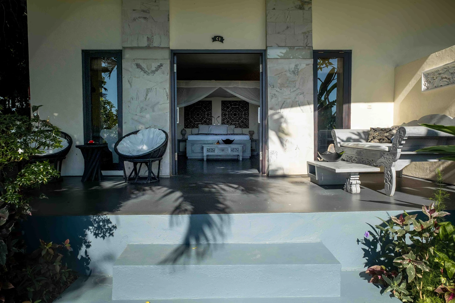 Premium villa private balcony with modern chairs and bench leading to bedroom with a canopy bed and decorative wall art.