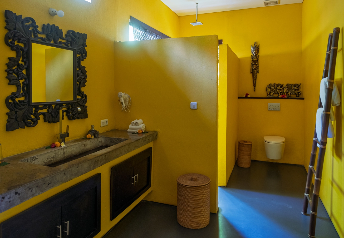 Premium villa spacious bathroom with a stone sink, ornate mirror, wicker basket, toilet, and bamboo towel rack.