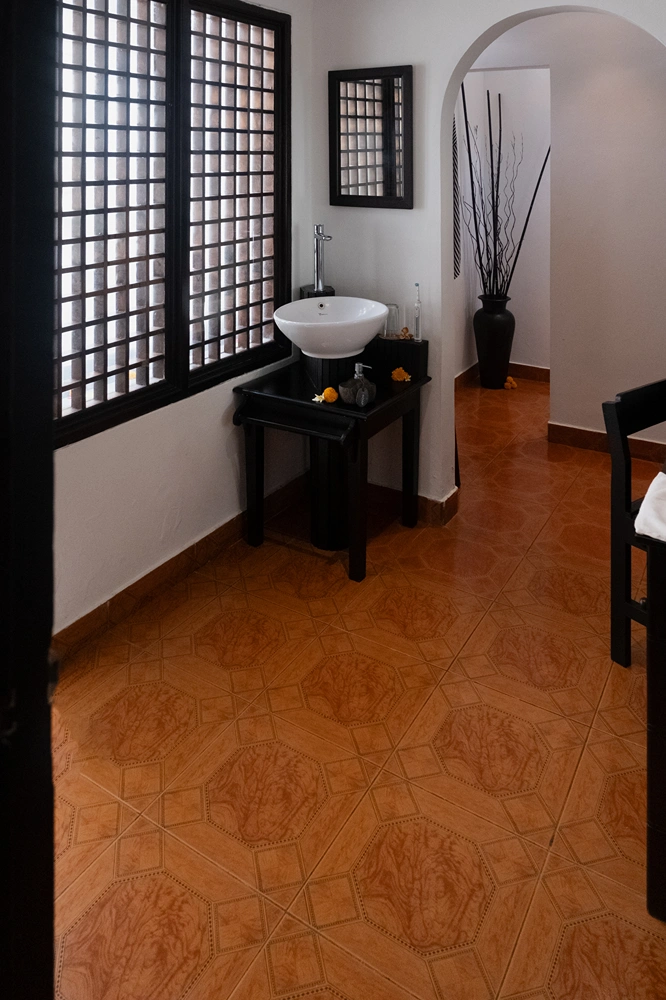 Sunrise villa spacious bathroom with a small white basin, black stand, large window with grid, and a black vase with sticks.
