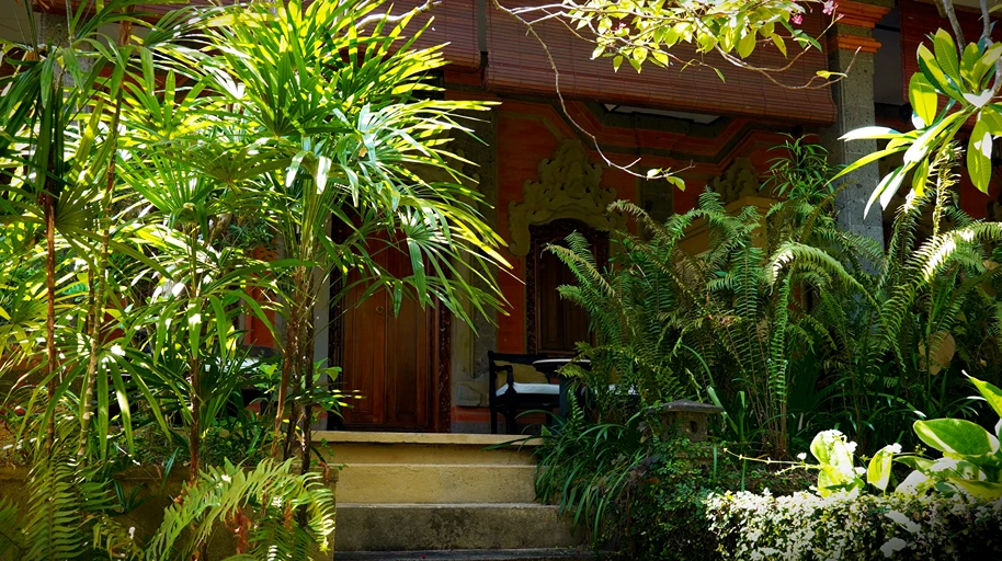 Gardens in front of sunset villa leading to a wooden doorway with carved details.