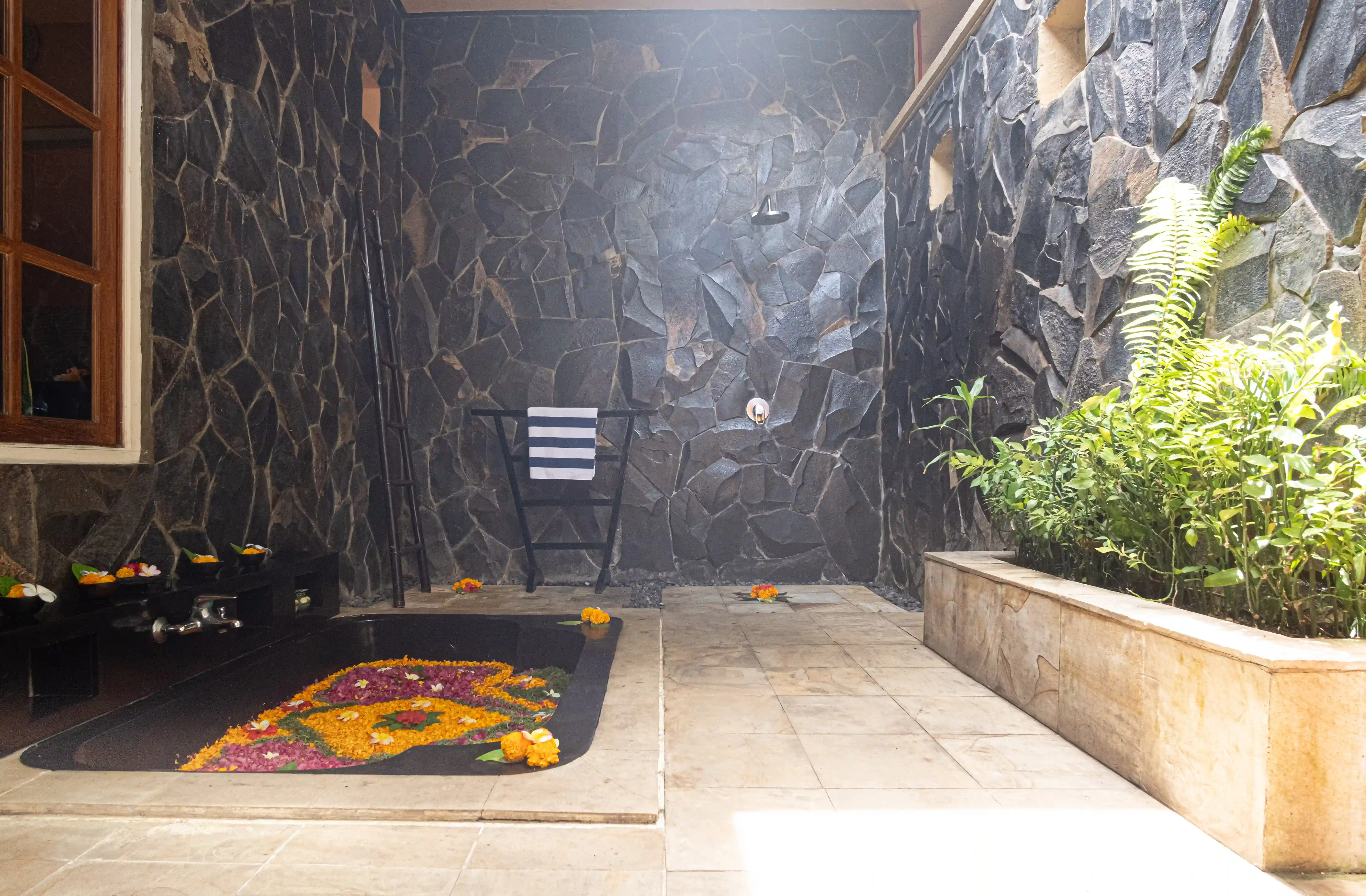Sunset villa open air bathroom with flower decorations, stone walls, a towel rack, and a planter with green plants.