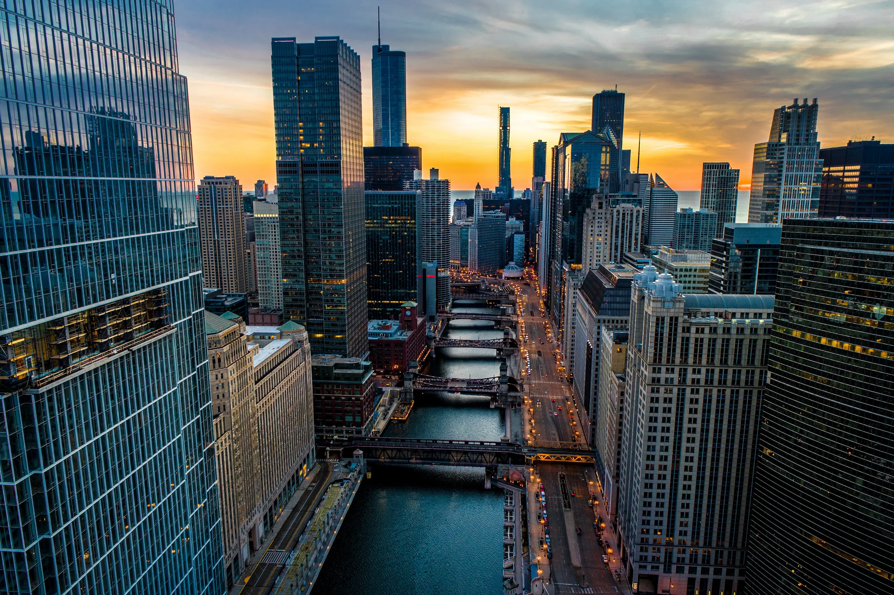 Aerial view of a city river with bridges and tall buildings at sunset with orange sky.