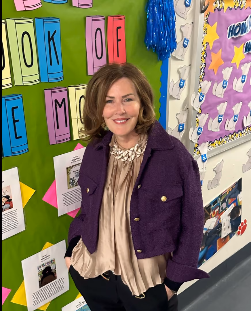 Principal smiling in front of colorful school hallway bulletin boards