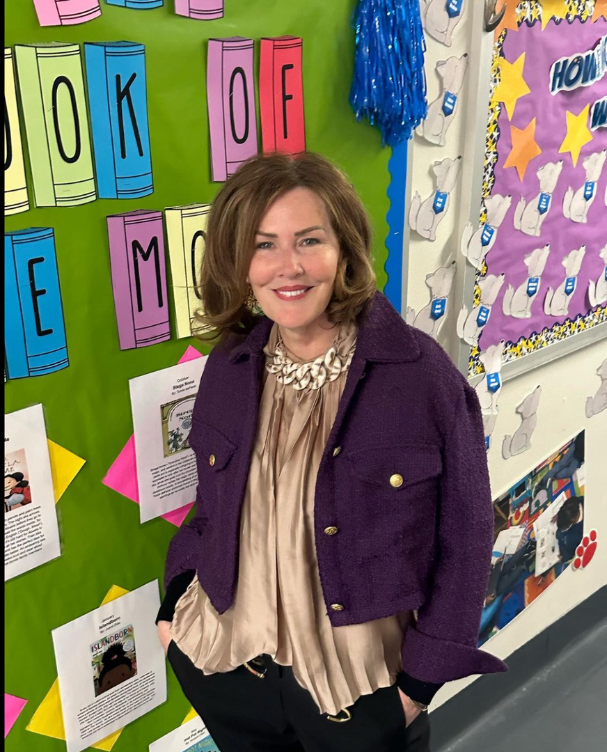 Principal smiling in front of colorful school hallway bulletin boards