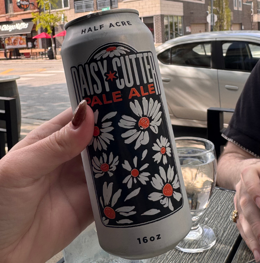 Hand holding a 16oz can of Half Acre Daisy Cutter Pale Ale with daisy illustrations outdoors.