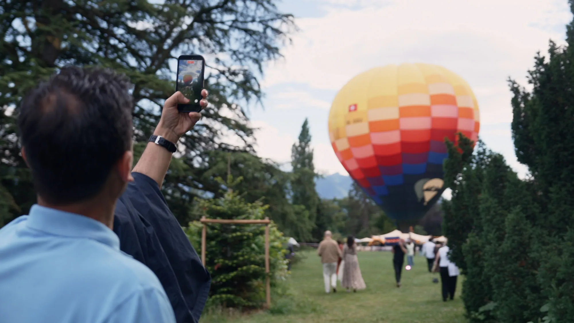 Un invité filme au téléphone une montgolfière gonflée dans le parc d’un événement en plein air